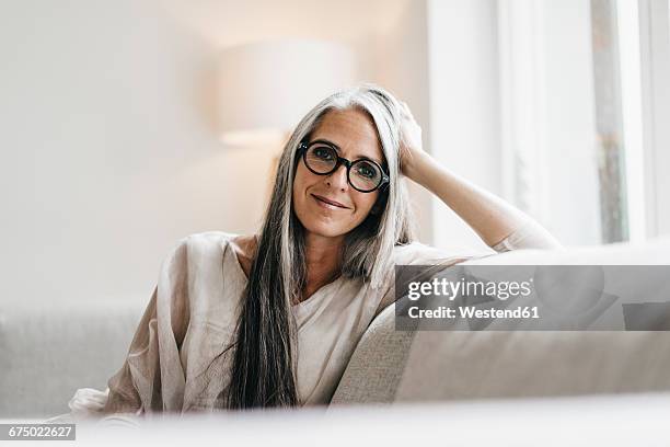 portrait of smiling woman with long grey hair sitting on the couch - hair woman mature grey hair beauty stockfoto's en -beelden
