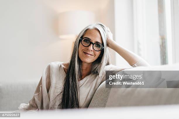 portrait of smiling woman with long grey hair sitting on the couch - one grey hair stock pictures, royalty-free photos & images