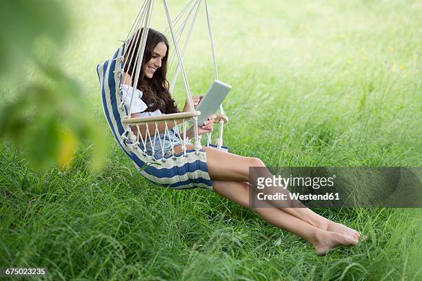 happy woman with tablet relaxing in a hanging chair on a meadow - hanging chair stock pictures, royalty-free photos & images