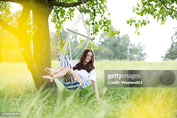 happy woman relaxing in a hanging chair under a tree - barefoot women stock-fotos und bilder