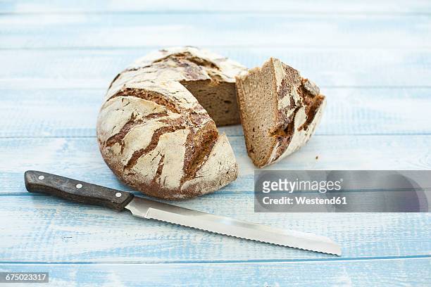 rustic rye bread on blue wood, knife - roggebrood stockfoto's en -beelden