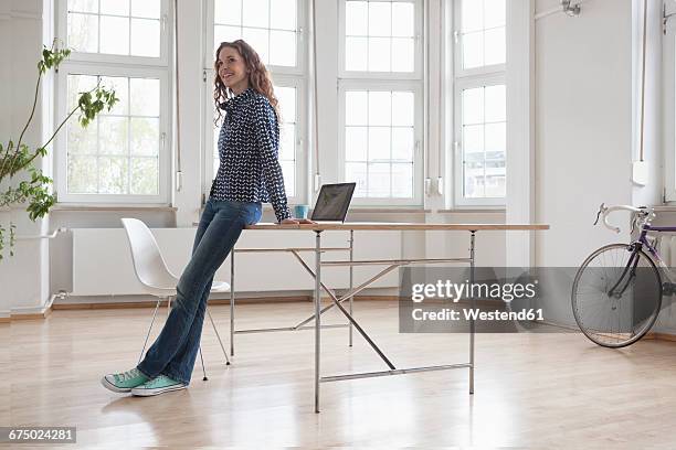 smiling woman in sparse office - anlehnen stock-fotos und bilder