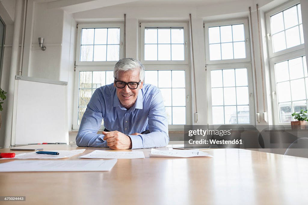 Portrait of confident mature businessman leaning on table in conference room