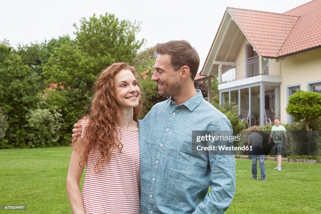 Smiling couple in garden with kids in background