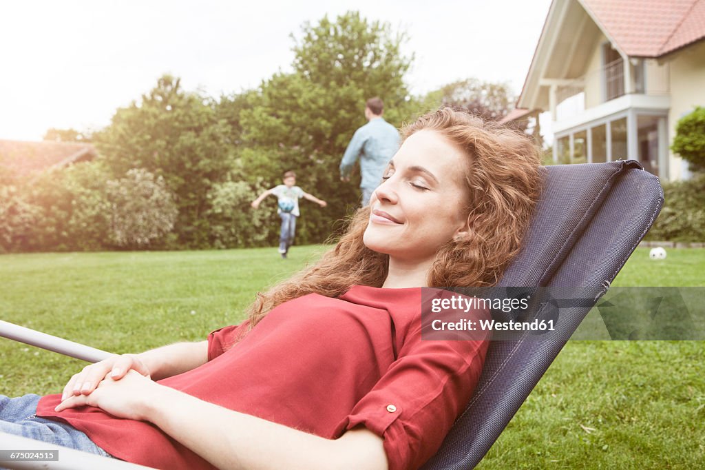 Woman relaxing in deckchair in garden with family in background