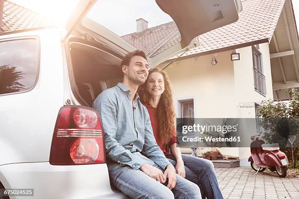 smiling couple sitting in car trunk at house - middle class female stock pictures, royalty-free photos & images