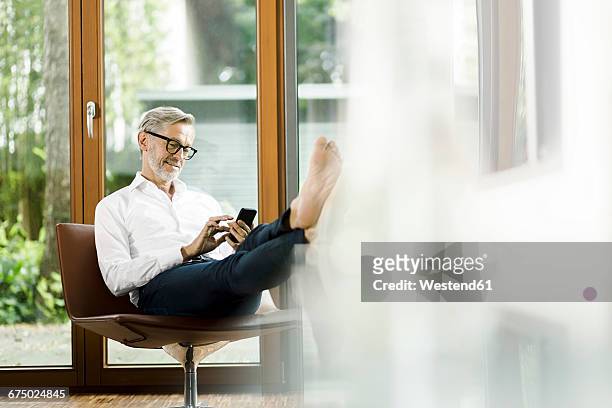 man sitting on chair in his living room text messaging - rijk stockfoto's en -beelden