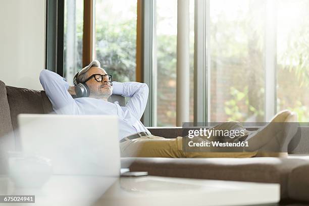 man relaxing on the couch listening music with headphones - einfaches leben stock-fotos und bilder