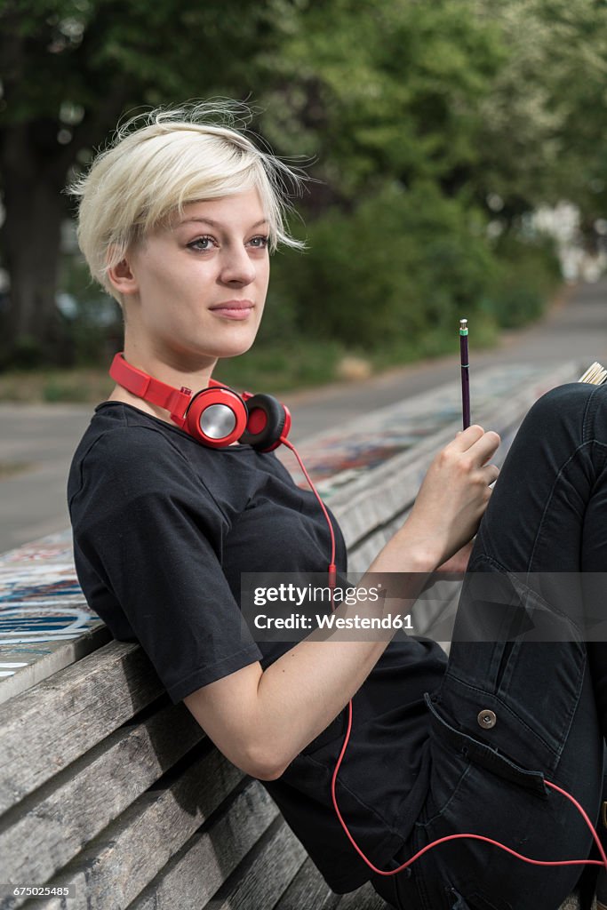 Portrait of young woman with headphones drawing on park bench