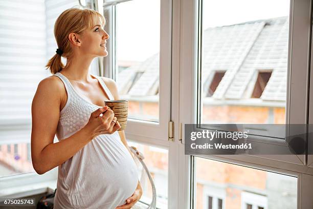 pregnant woman holding her belly, looking through window - pregnant coffee 個照片及圖片檔