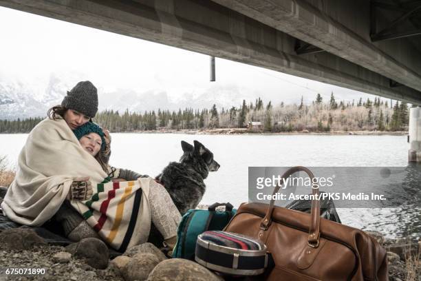 mother and daughter huddle at roadside, with belongings - homelessness stockfoto's en -beelden
