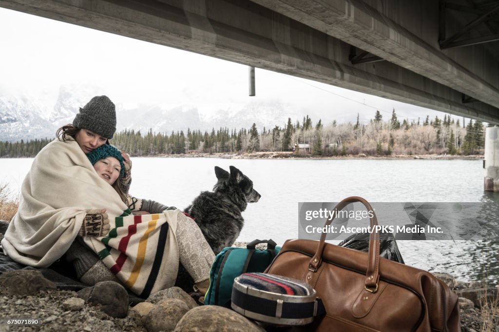 Mother and daughter huddle at roadside, with belongings