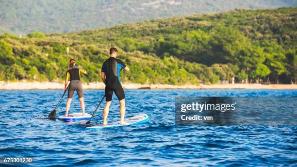 two paddle boarders rowing towards the coast - paddle board men imagens e fotografias de stock