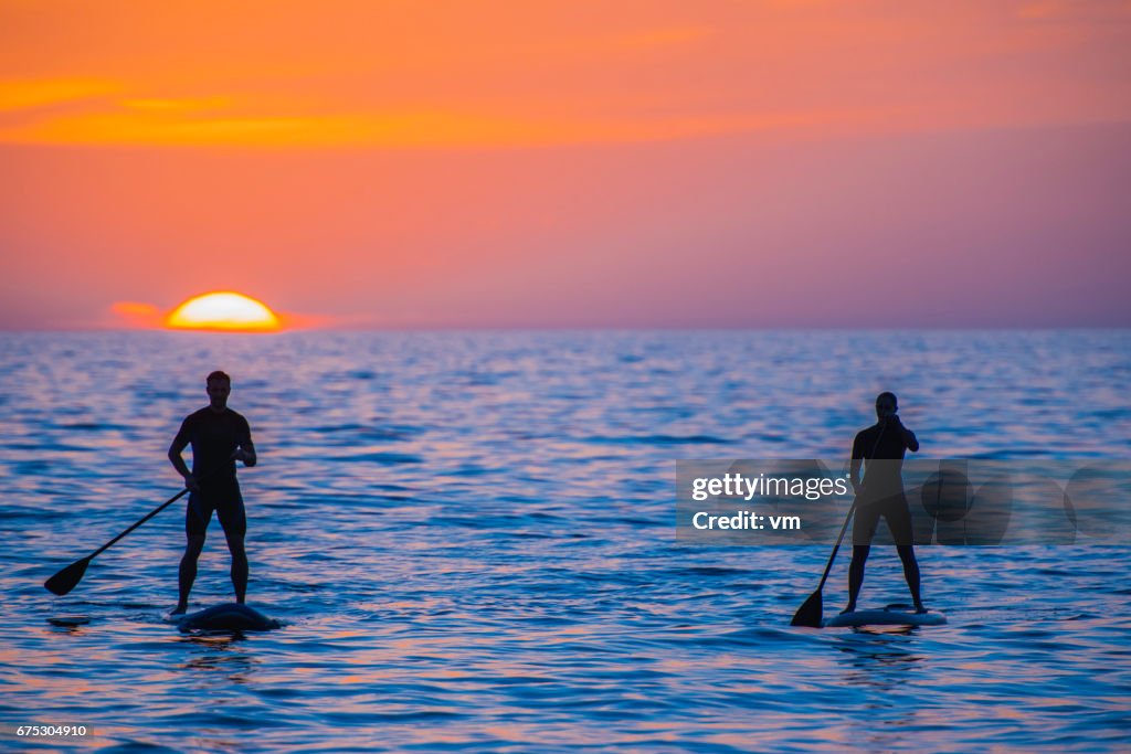 Peddelen boarder paar op zee tijdens zonsondergang