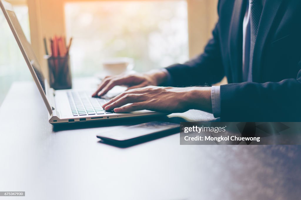 Hand of businessman using his laptop with a cup of coffee on office desk. Portrait of business man using laptop in office.