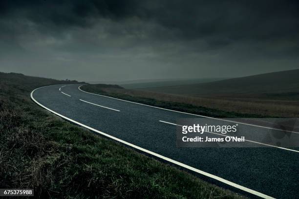 curved road through stormy landscape - carretera vacía fotografías e imágenes de stock
