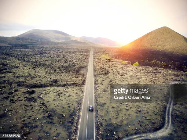 imagen aérea de un coche conduciendo por una carretera en lanzarote, españa. - carretera paisaje vista aerea fotografías e imágenes de stock