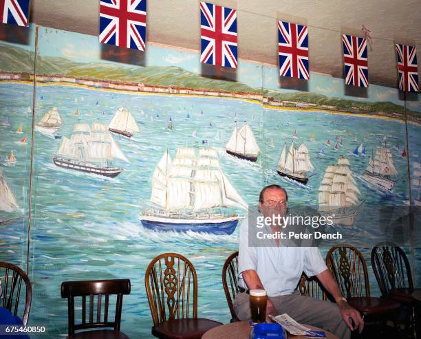 Man sits with a full pint of Guinness in front of a nautical-themed painted wall in a bar on the Esplanade in the seaside town of Weymouth. Dorset....