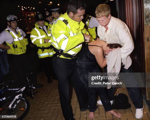 Woman in distress on a night out in Basingstoke town centre is helped to her feet by a police officer. September 2004.