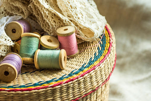 Woven rattan crafts and sewing supply box, wooden spools, rolls of lace, linen cloth background, hobby fashion concept