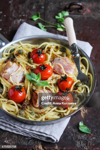 spaghetti pasta with roasted cherry tomatoes, bacon slices, capers and herbs in a pan ready to serve, selective focus - spiral ham stock pictures, royalty-free photos & images