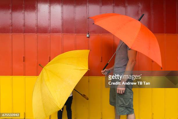 a man and a child with a yellow and orange umbrellas, the matching colours for the painted gate behind. - camouflage photography stock-fotos und bilder