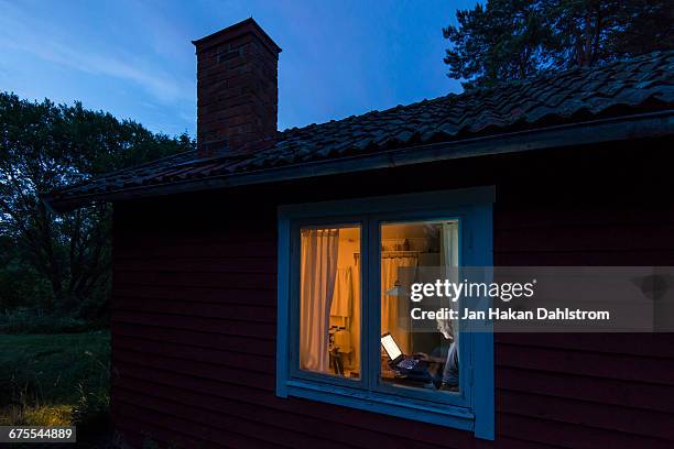 man working in cottage window - house dusk stock pictures, royalty-free photos & images