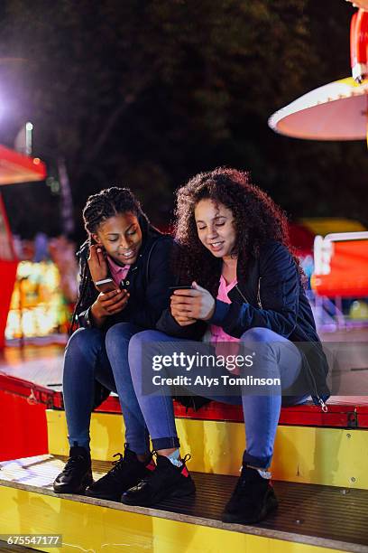two teenage girls texting at fairground - unfilteredtrend stock pictures, royalty-free photos & images