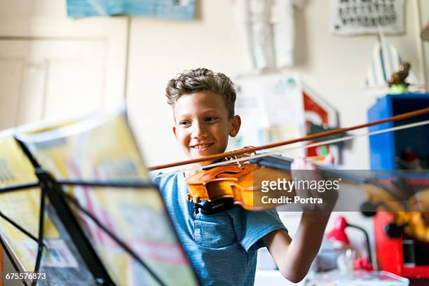smiling boy playing violin in domestic room - kids instruments stock-fotos und bilder