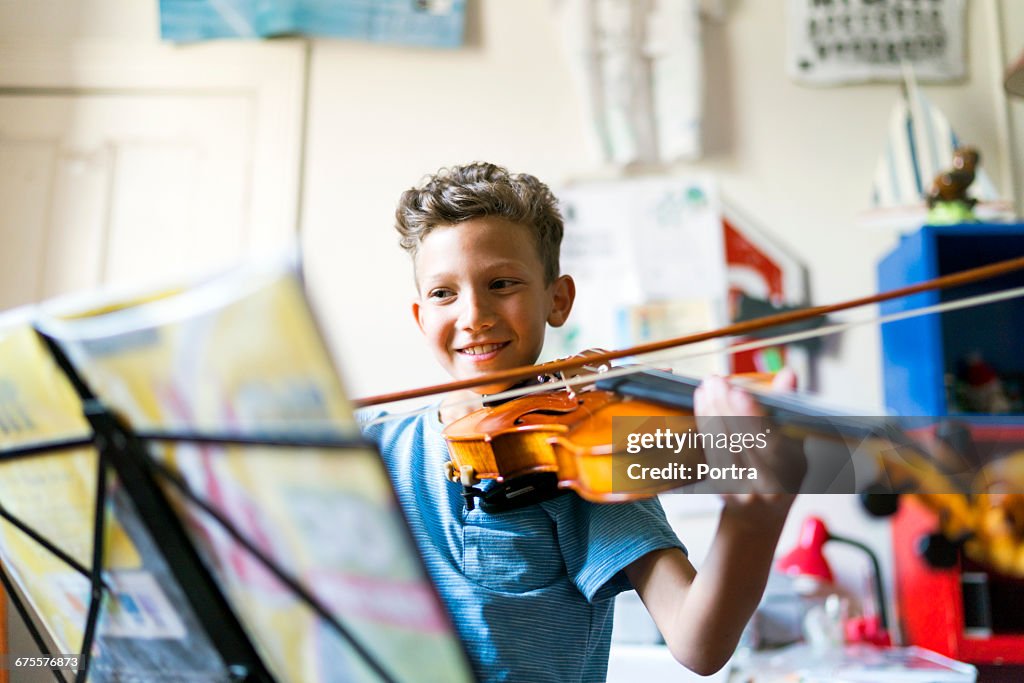 Smiling boy playing violin in domestic room