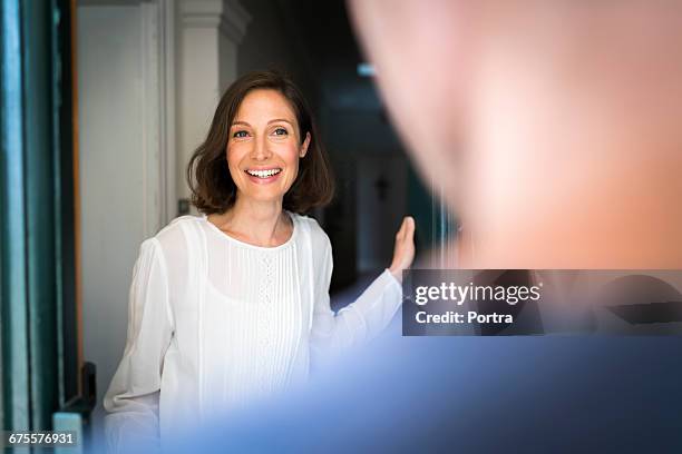 smiling mid adult woman standing on entrance - opening door foto e immagini stock