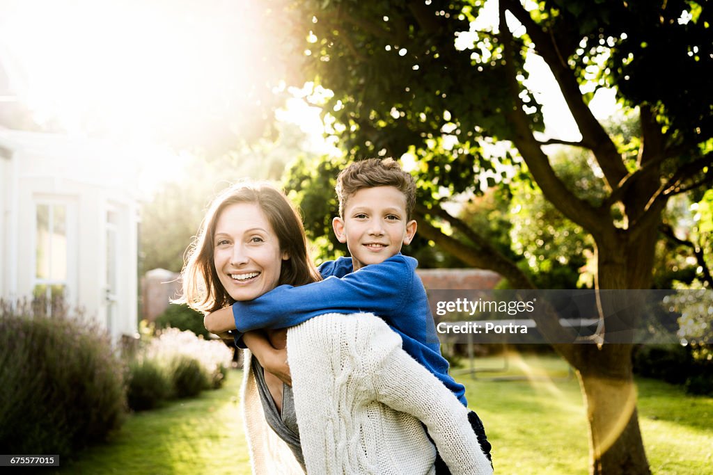 Portrait of woman piggybacking son in yard