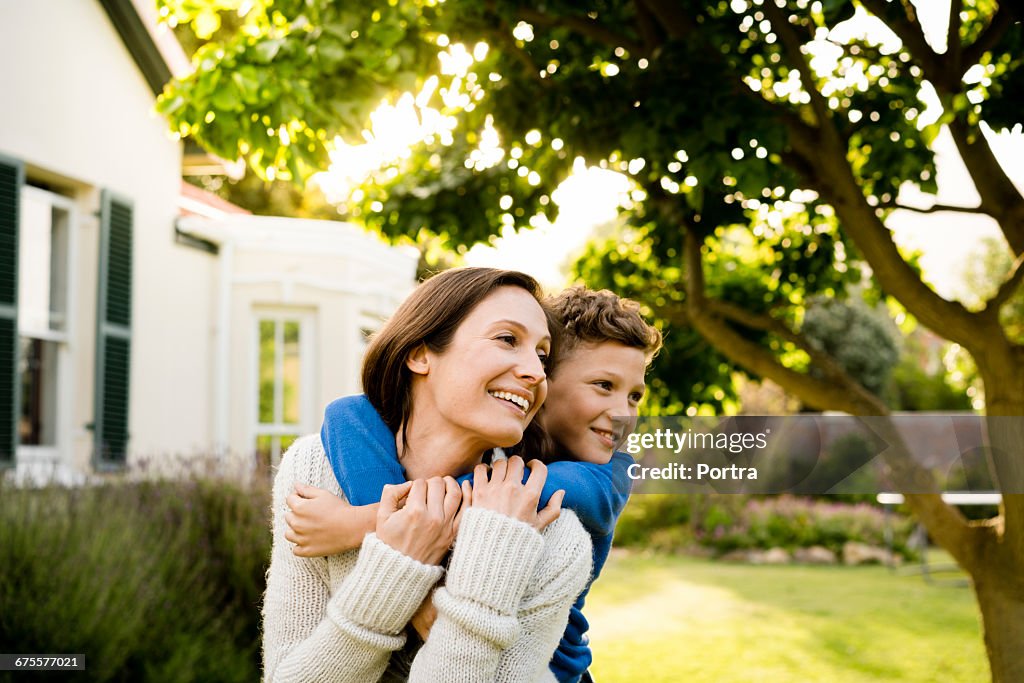 Boy embracing mother outside house in yard