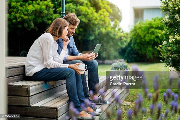 couple using digital tablet while sitting on steps - tablet couple stock pictures, royalty-free photos & images
