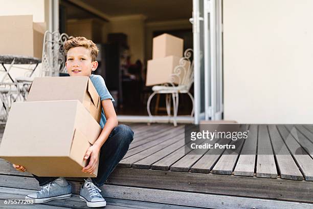 portrait of smiling boy with boxes at porch - boy in a box stockfoto's en -beelden