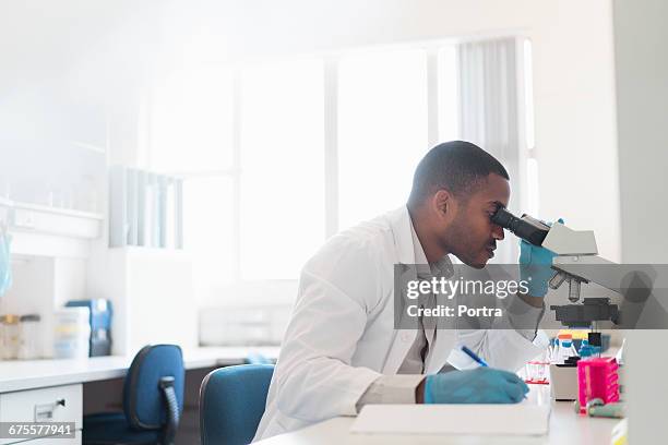 chemist analyzing through microscope at laboratory - cientifico con microscopio fotografías e imágenes de stock
