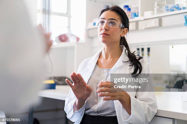 scientist gesturing while discussing at laboratory - scientifique blouse blanche photos et images de collection