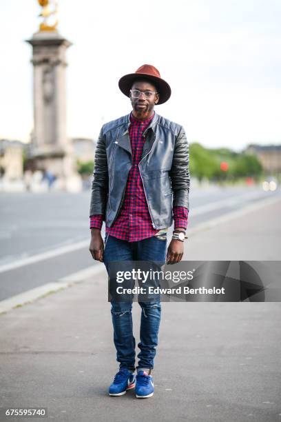 Sidya Sarr wears a Zara red tartan shirt, an Asos leather black jacket, Nike Cortez blue sneakers shoes, a Zara hat, Asos blue denim ripped jeans,...