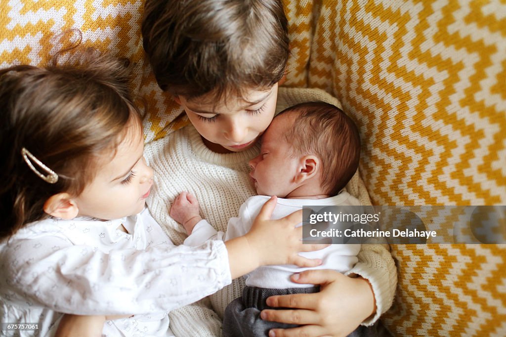 A baby in the arms of his big brother and sister