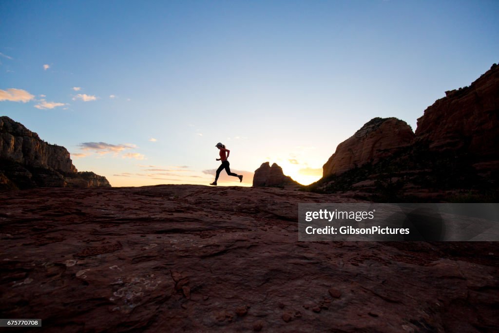 A woman goes for a cross-country trail run at sunset in Sedona, Arizona, USA.
