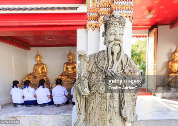kids in uniforme are praying in a temple in thailand in front of statue of buddha - sac à dos stock-fotos und bilder