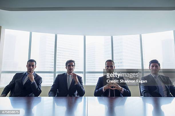 row of businessmen sitting at conference table - four bussines man at office imagens e fotografias de stock