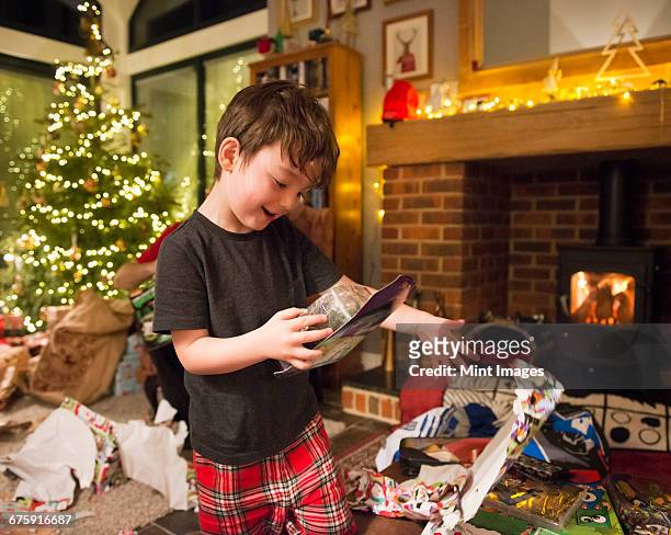 a boy opening his presents on christmas day throwing the wrapping paper to the floor. - christmas toys stock pictures, royalty-free photos & images