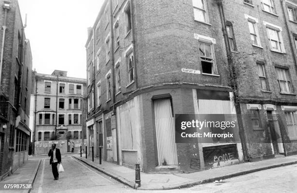 Man carrying his shopping bag as he walks past delapidated buildings with broken windows and boarded up doorways in the streets around Cannon Street,...