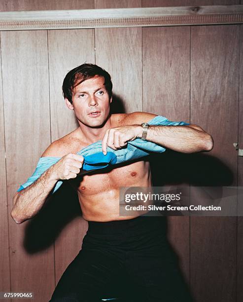 American actor Adam West puts on a t-shirt, circa 1965.