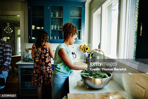 friends preparing dinner together in kitchen - leaf vegetable stock pictures, royalty-free photos & images