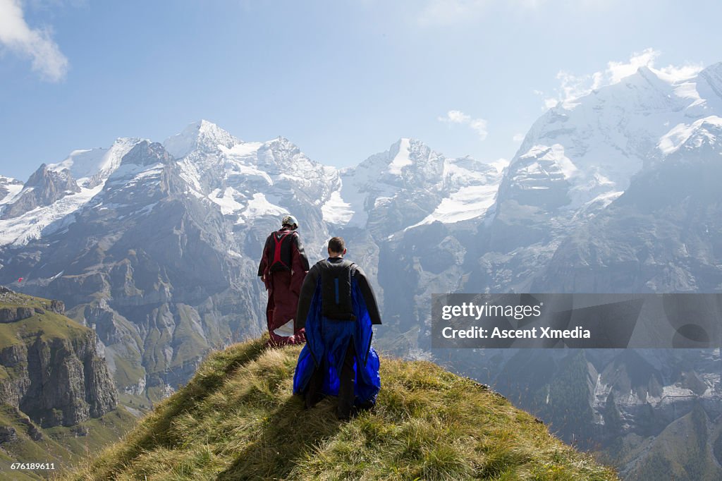 Wingsuit fliers prepare to jump from grassy crest