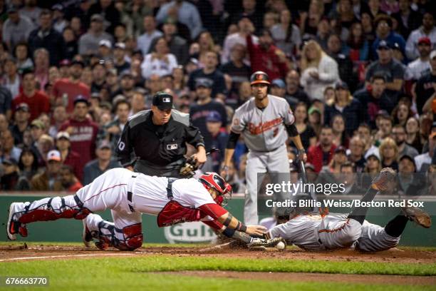 Jonathan Schoop of the Baltimore Orioles slides as he evades the tag of Sandy Leon of the Boston Red Sox to score during the fifth inning of a game...