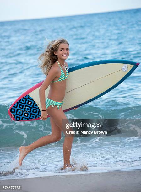 young gril walking in the surf with surf board. - tween girl swimsuit stock-fotos und bilder