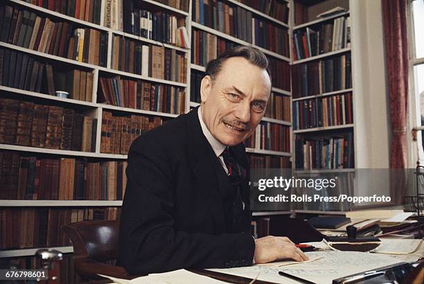 British Conservative Party politician and Member of Parliament for Wolverhampton South West, Enoch Powell pictured sitting at a desk in his library...